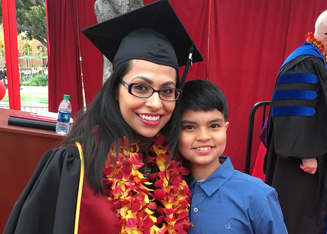 Jessica Flores, wearing graduation garb, smiling with her son
