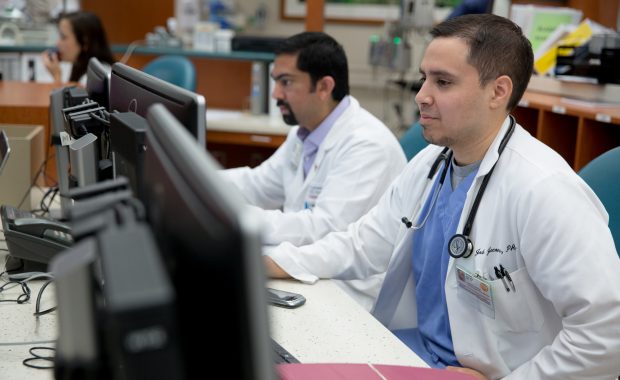 Two men in white coats working on computers