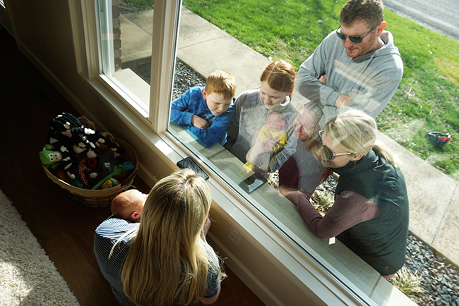 Braedon Haertling y su familia visitando a su esposa y recién nacido a través de la ventana de vidrio