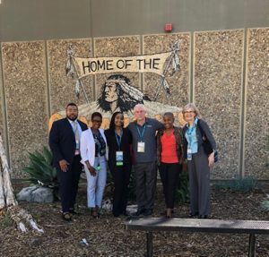 Six educators stand in front of a high school