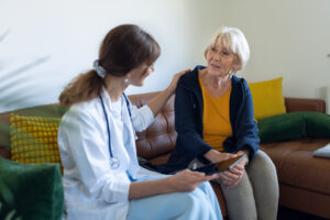 A female family doctor is checking on the condition of a female patient at home. She measures her blood pressure, the patient is calm and a little worried. She speaks to her calmly and positively.