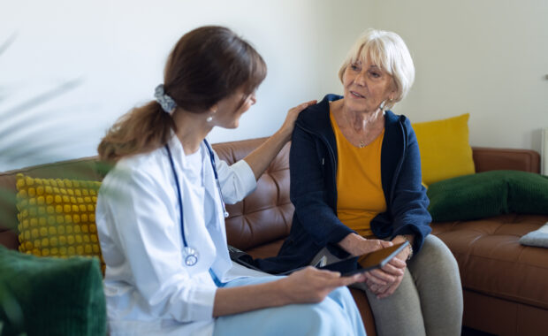 A female family doctor is checking on the condition of a female patient at home. She measures her blood pressure, the patient is calm and a little worried. She speaks to her calmly and positively.